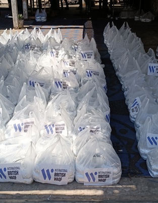 هل إطعام الطعام صدقة جارية امرأة تتسلّم صندوق طعام للأضاحي 2024 من متطوع خلال فعالية توزيع في الهند، بتنظيم الوقف البريطاني الدولي وتنفيذ Human Appeal. تظهر في الخلفية صناديق بنفسجية ولافتات.