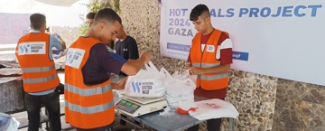 فوائد الوقف الخيري متطوعون يرتدون سترات برتقالية يعبئون ويوزعون أكياس الطعام ضمن مشروع وجبات ساخنة إنساني.